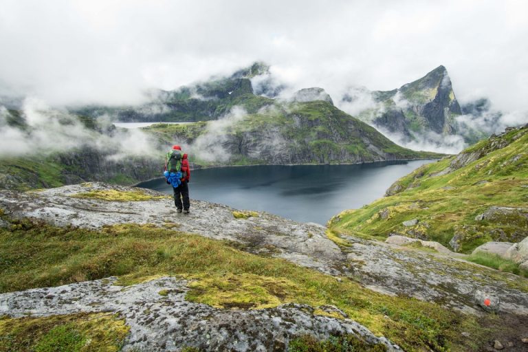 hiker-standing-beside-lake-lofoten-mountains-foggy-day