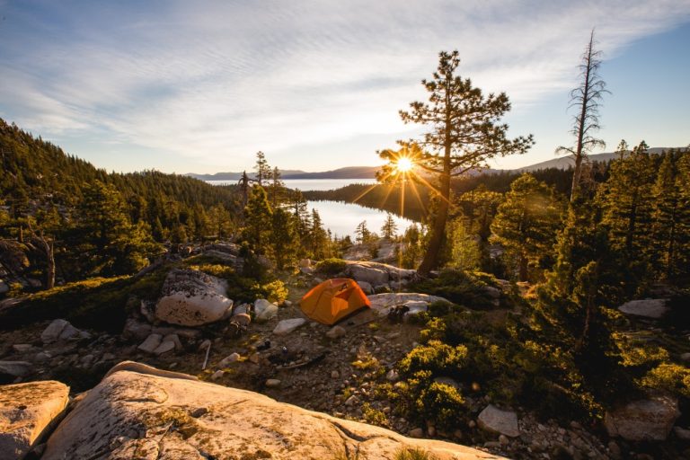 beautiful-shot-orange-tent-rocky-mountain-surrounded-by-trees-during-sunset